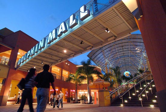 A shopping couple walks under the neon entrance sign at the Dolphin Mall in Miami, Florida.