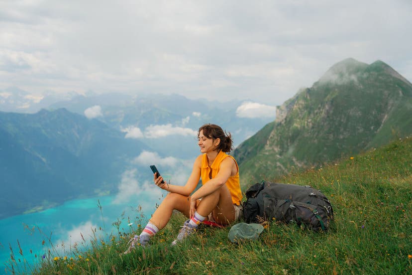 Woman sitting on the meadow in Swiss Alps overlooking Interlaken and using smartphone during the hike in summer