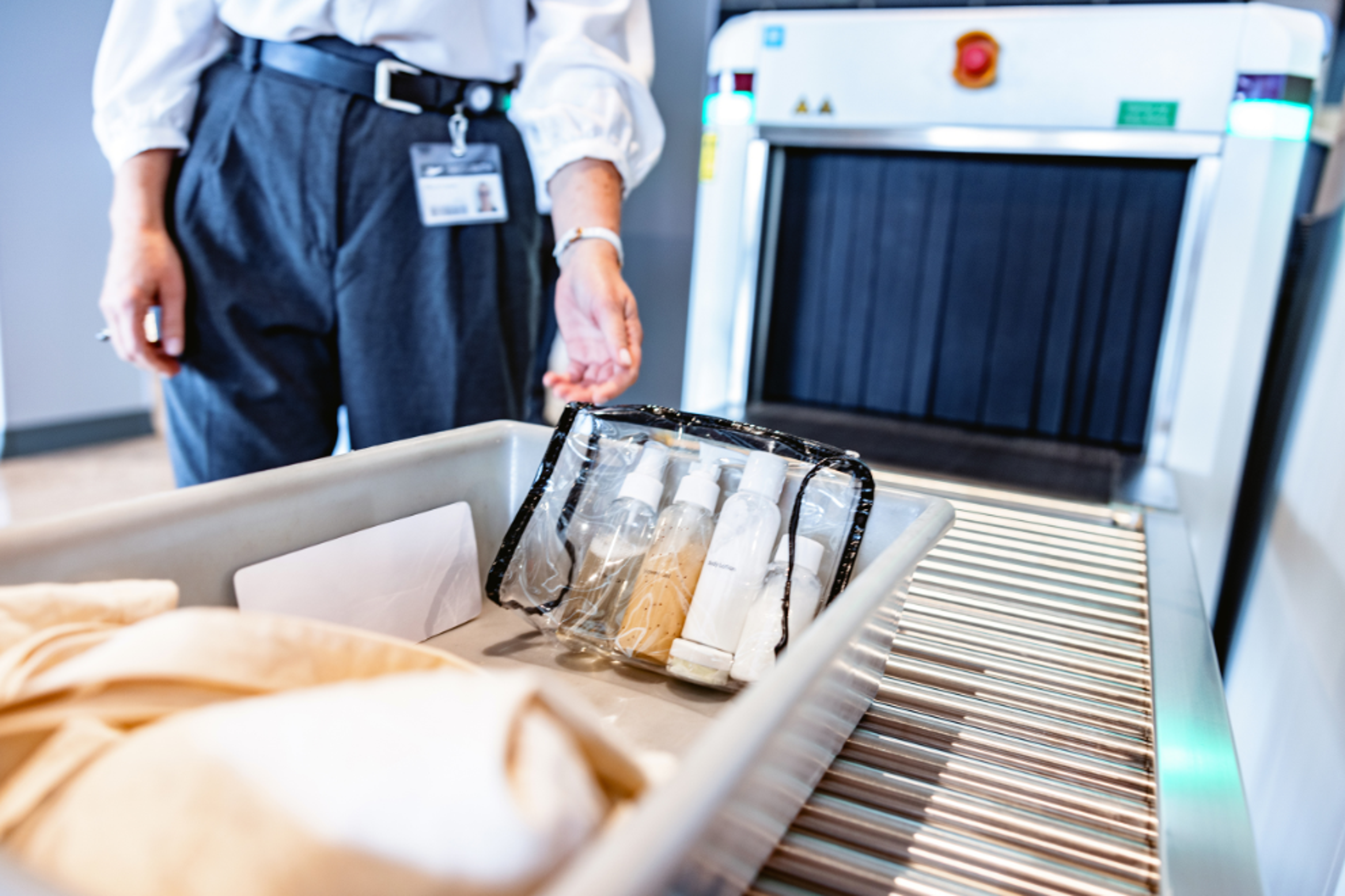 Close up shot of a tray filled with liquid toiletries in a clear zip top bag. The tray is on a roller conveyors table and is ready for a x-ray scan.